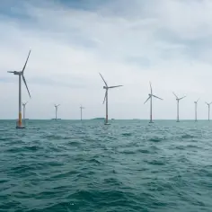 Wielkie turbiny wiatrowe na morzu, symbol nowoczesnej morskiej energetyki wiatrowej, na tle błękitnego nieba i falującego oceanu.