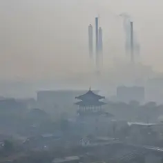 Smog nad miastem z tradycyjną architekturą i kominami fabryk emitującymi dym.