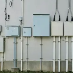 Rozbudowany system skrzynek i rur na ścianie, przygotowany do podłączenia prądu do działki bez domu.
