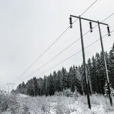 Zimowy krajobraz z linią wysokiego napięcia przecinającą zaśnieżony las.