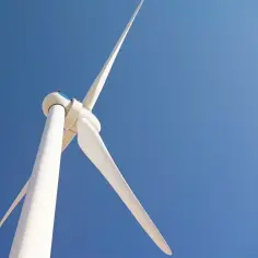 Białe turbiny wiatrowe obracają łopatami na tle błękitnego nieba, czerpiąc energię z wiatru.
