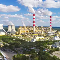 Największa elektrownia w Polsce z charakterystycznymi kominami i chłodniami, otoczona zielenią.