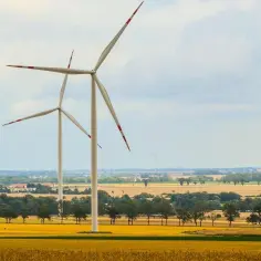 Wiatraki na tle pól i chmur, symbolizujące czystą energię wiatru.