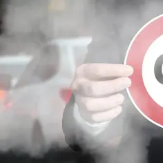 Dłoń trzyma znak z napisem CO2 na tle dymiących samochodów.