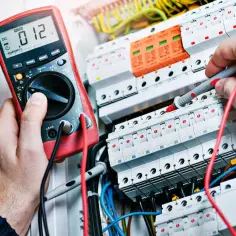Elektryk z uprawnieniami G1 sprawdza napięcie multimetrem w skrzynce z bezpiecznikami.