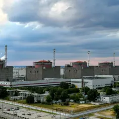 Ogromna elektrownia jądrowa Zaporoże z sześcioma blokami energetycznymi pod czerwonymi kopułami, otoczona zielenią i parkingiem z samochodami.