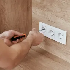 Ręce przykręcają gniazdko elektryczne. Elektryk dba o prawidłową wartość skuteczną napięcia w instalacji.