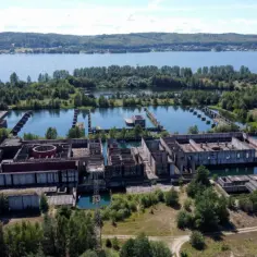 Niedokończona elektrownia w Żarnowcu, otoczona wodą i zielenią, z widokiem na jezioro w tle.