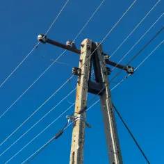 Słup energetyczny z przewodami na tle błękitnego nieba. Dowiedz się, ile wynosi odszkodowanie za słupy energetyczne na działce.