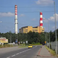 Dwa wysokie kominy PGE Stalowa Wola górują nad krajobrazem. Obok budynki przemysłowe i droga.