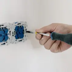 Ręka przykręca gniazdko elektryczne. To ważny etap prac, który zapewnia prawidłowy pomiar rezystancji izolacji instalacji.