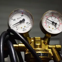 Dwa manometry na mosiężnym regulatorze PID pokazują ciśnienie w barach i przepływ w l/min.