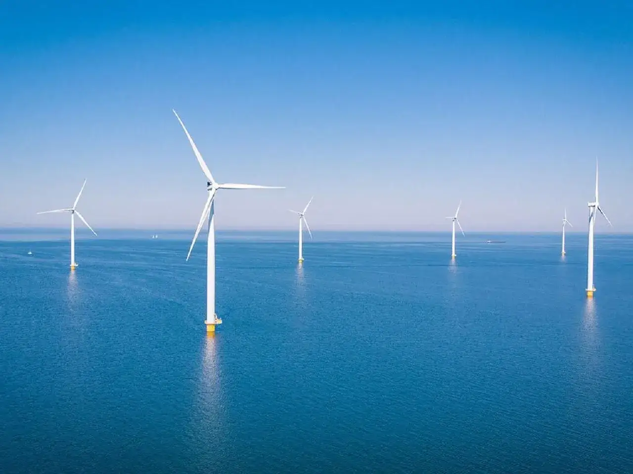 Farma wiatrowa na Bałtyku. Białe turbiny na tle błękitnego nieba i morza, czerpią energię z wiatru.