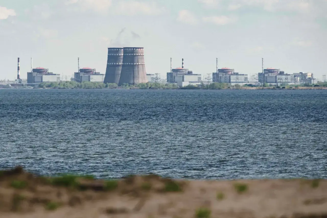 Ogromna elektrownia jądrowa Zaporoże z charakterystycznymi chłodniami kominowymi, widoczna zza wody.