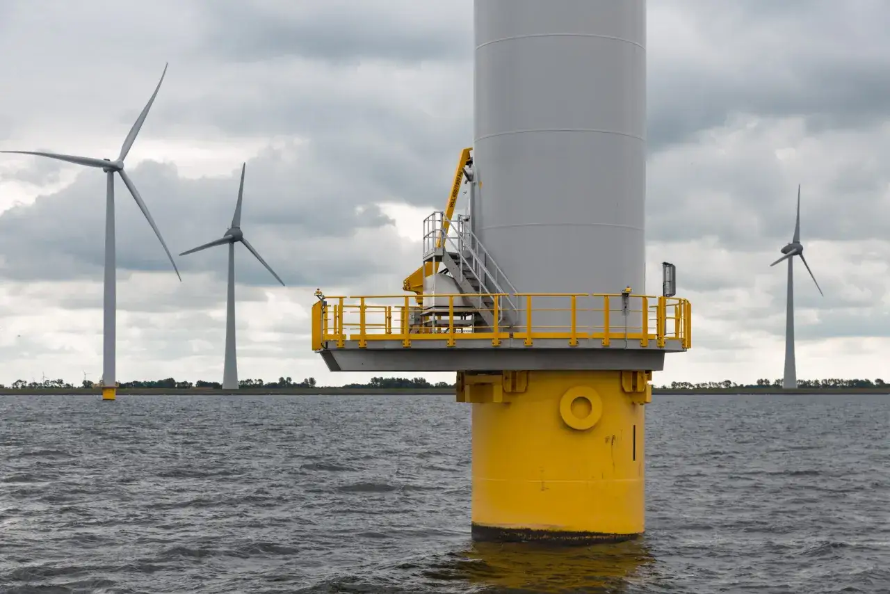 Wielkie turbiny wiatrowe na morzu, symbol nowoczesnej morskiej energetyki wiatrowej, na tle pochmurnego nieba.