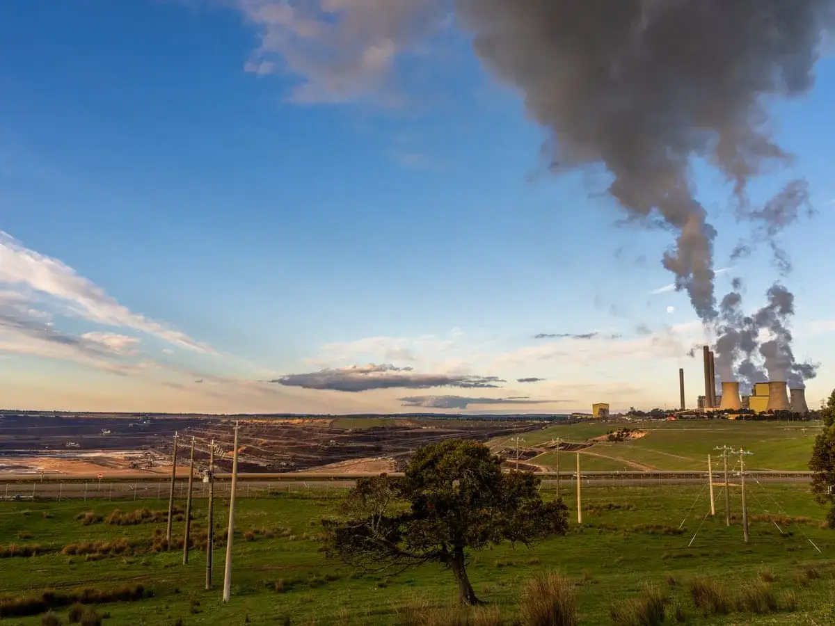Kopalnia odkrywkowa i elektrownia emitująca dym, symbolizujące wykorzystanie paliw kopalnych.
