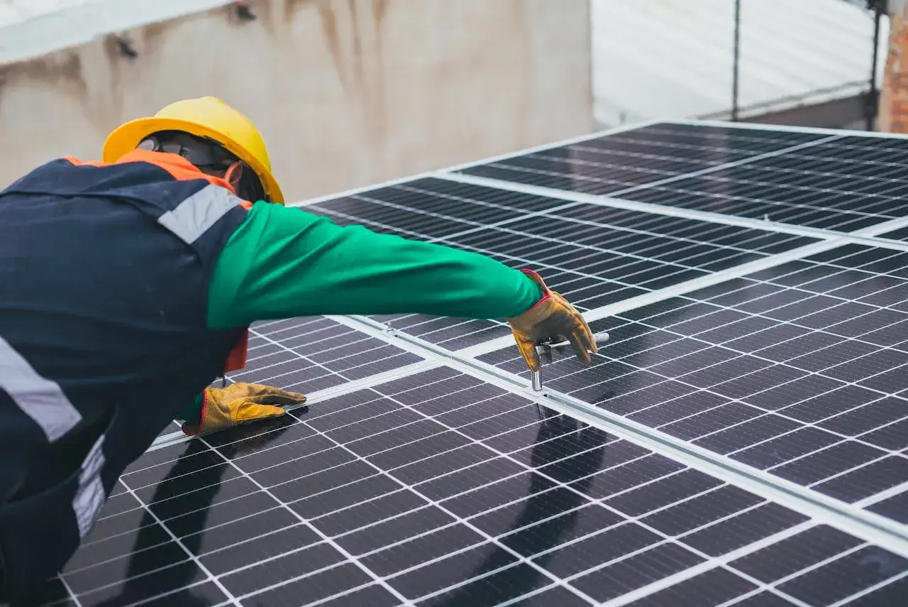 Pracownik w żółtym kasku montuje panele słoneczne. Posiada uprawnienia G1 do pracy przy instalacjach elektrycznych.