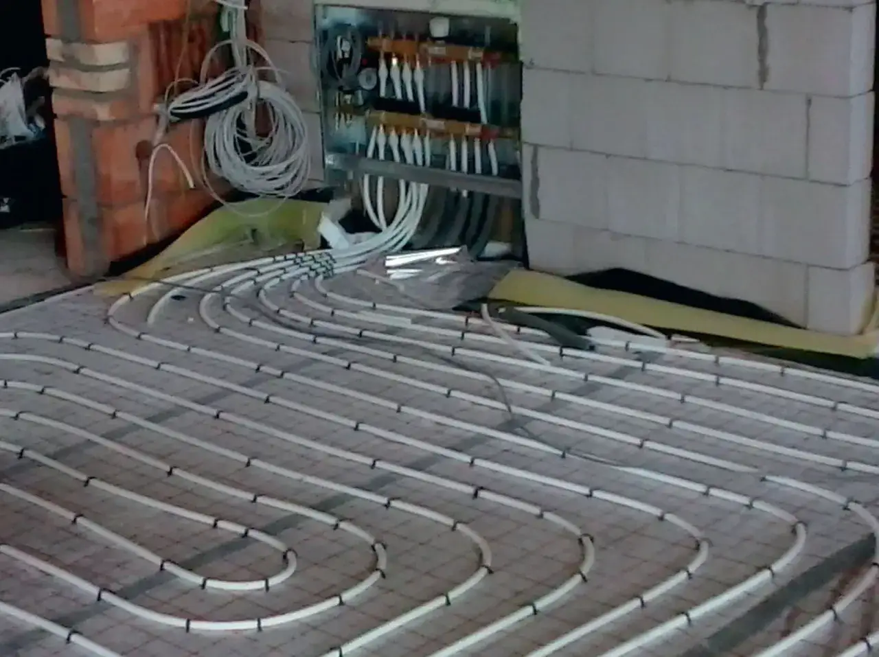 Instalacja ogrzewania podłogowego. Rury ułożone w pętle na siatce, podłączone do rozdzielacza. To rozwiązanie obniża koszt ogrzewania.