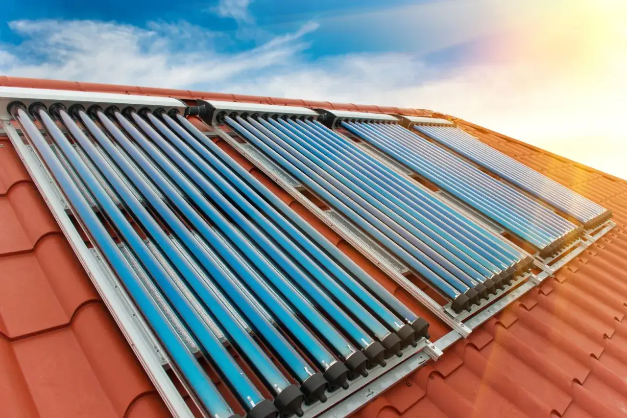 Instalacja solarna na dachu z niebieskimi kolektorami rurowymi, łapiąca promienie słońca.